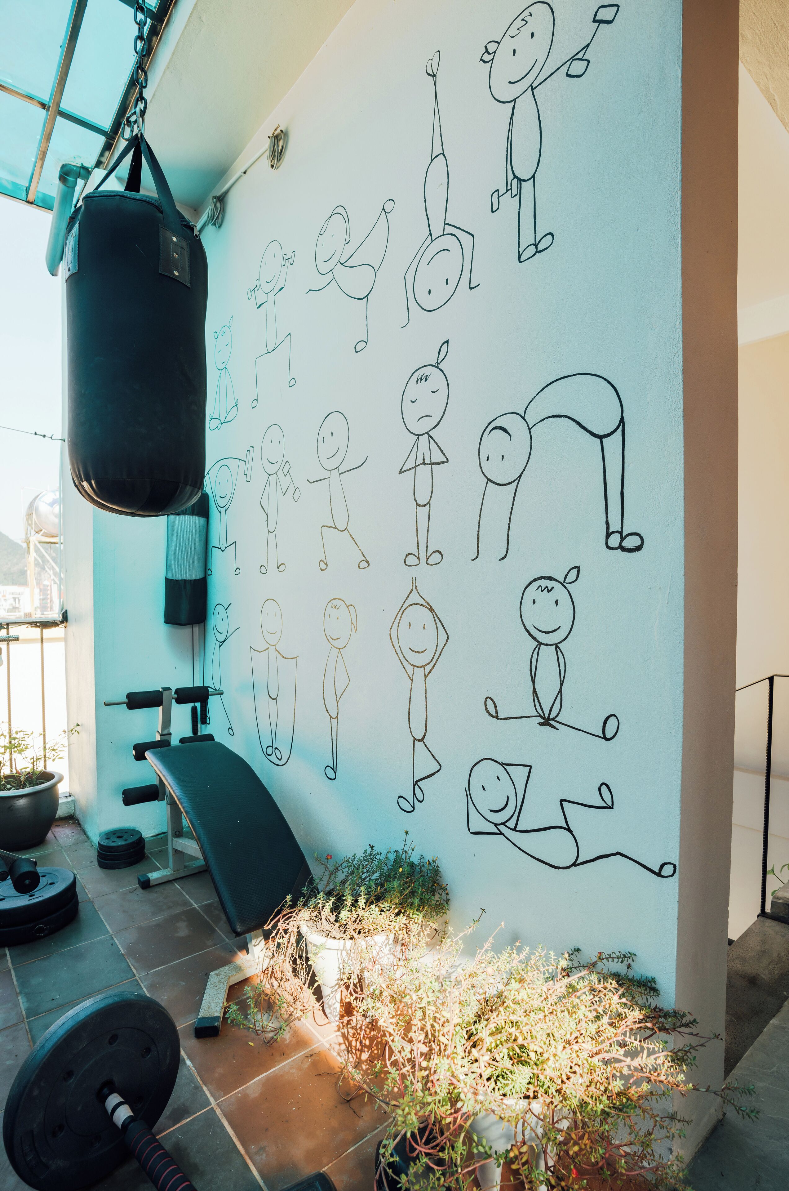 A gym with a punching bag, exercise equipment, and a wall with stick figure drawings of people exercising.