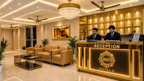 A reception area with a reception desk, two staff members, a chandelier, ceiling fans, and a large painting. - Hotel Urban Luxury by JMD Group  (New Delhi)