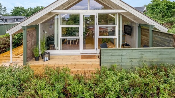 Una casa moderna con techo inclinado, amplios ventanales y una terraza de madera.