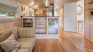 Un interior acogedor con techo de madera, un sofá, una zona de cocina con armarios y vistas por una ventana.