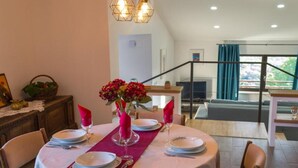 Un comedor con una mesa redonda preparada para cuatro, un florero con flores rojas y una escalera que lleva a un balcón.