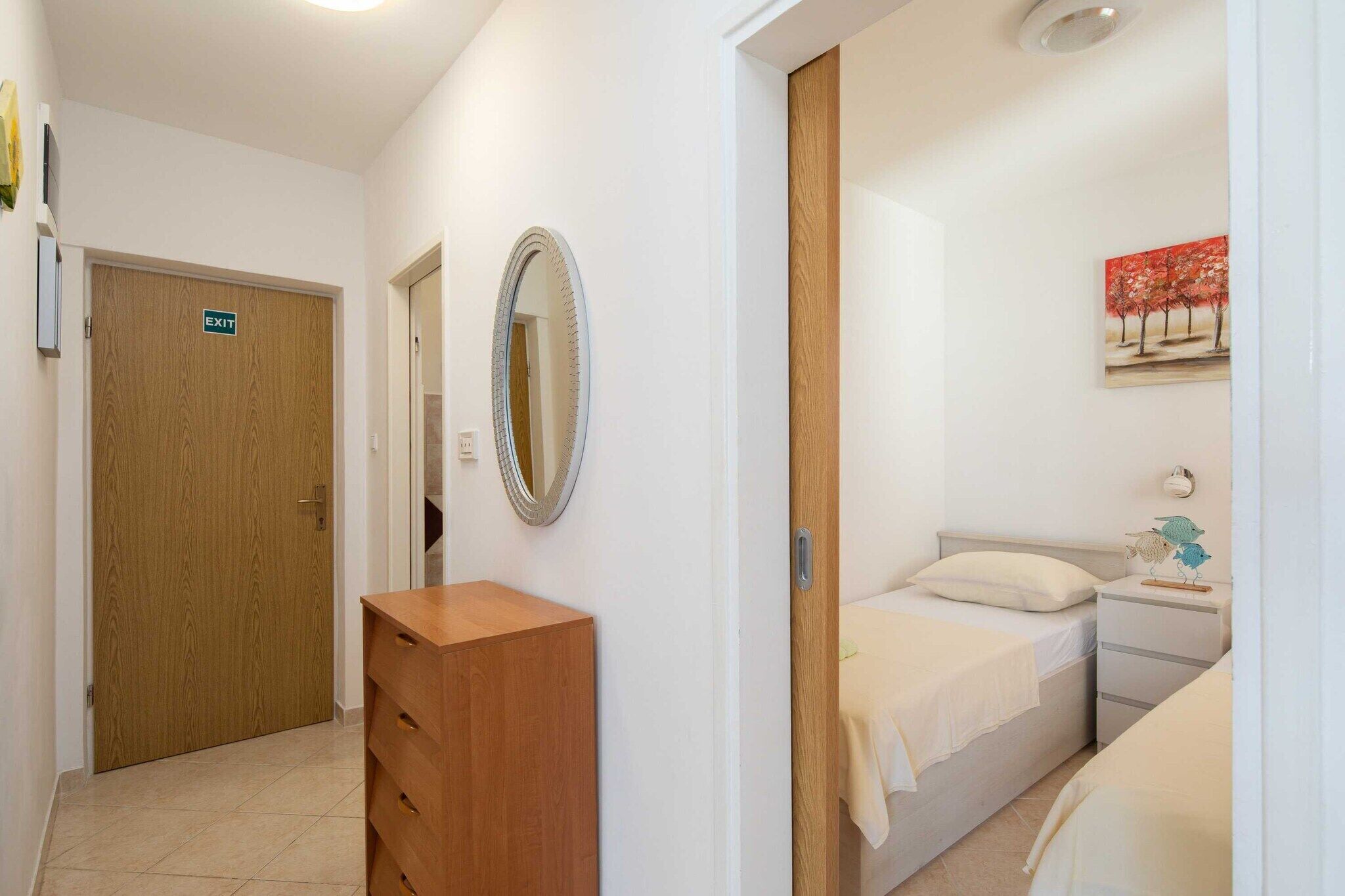 Hotelkamer met een houten garderobe, een bed met een witte matras en kussens, een nachtkastje met een lamp en een schilderij aan de muur.