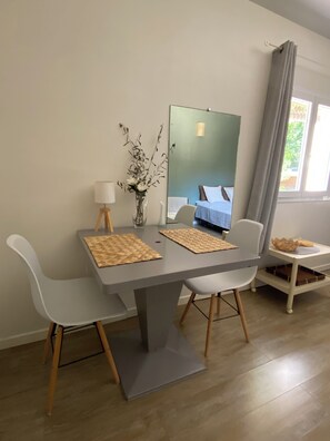 A modern dining area with a table, chairs, a vase with branches, a lamp, and a mirror reflecting a bed. - Detached studio with terrace in Aix countryside property (Aix-en-Provence)
