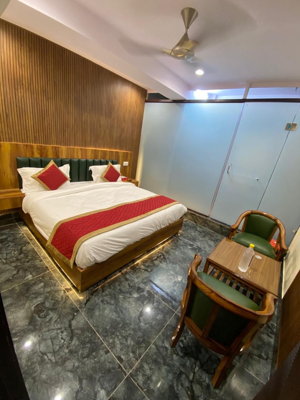 Una habitación de hotel con una cama grande, cabecero de madera, una silla tapizada de verde y una pequeña mesa de madera.