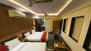 A hotel room with two beds, a ceiling fan, an air conditioner, a small table with a chair, and a view of the corridor. - Hotel Home Stay Residency (New Delhi)