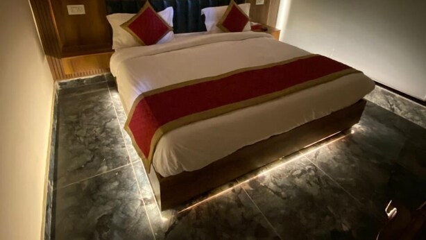A hotel room with a large bed, dark wooden headboard, and a red and white bedspread. - Hotel Home Stay Residency (New Delhi)
