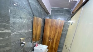 A bathroom with marble walls, wooden cabinets, a sink, and a shower. - Hotel Home Stay Residency (New Delhi)
