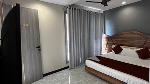 A modern bedroom with a bed, curtains, a ceiling fan, and a door. - Hotel Rajshree Inn (Ujjain)