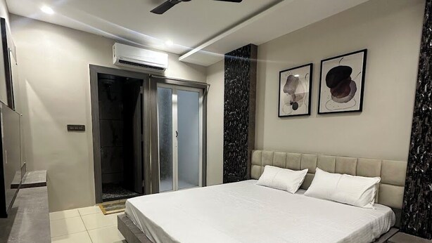 A modern bedroom with a large bed, a ceiling fan, and a door leading to a bathroom. - Hotel Rajshree Inn (Ujjain)