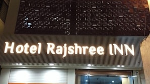 The exterior of Hotel Rajshree Inn with a prominent illuminated sign, a glass entrance, and a visible interior with a reception desk and seating area. - Hotel Rajshree Inn (Ujjain)