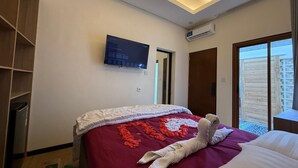 Ein modernes Hotelzimmer mit einem Bett, einem Flachbildfernseher, einer Klimaanlage und einer Glastür zum Außenbereich.
