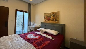 Ein Hotelzimmer mit einem Bett, einem Nachttisch, einem Gemälde und Blick auf ein Gebäude durch eine Glastür.