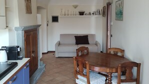 A dining area with a wooden table and chairs, a sofa, and a kitchen area with cabinets and a coffee maker. - Dimora Fenni – Historic elegance and modern comfort in the heart of Monte Isola (Monte Isola)