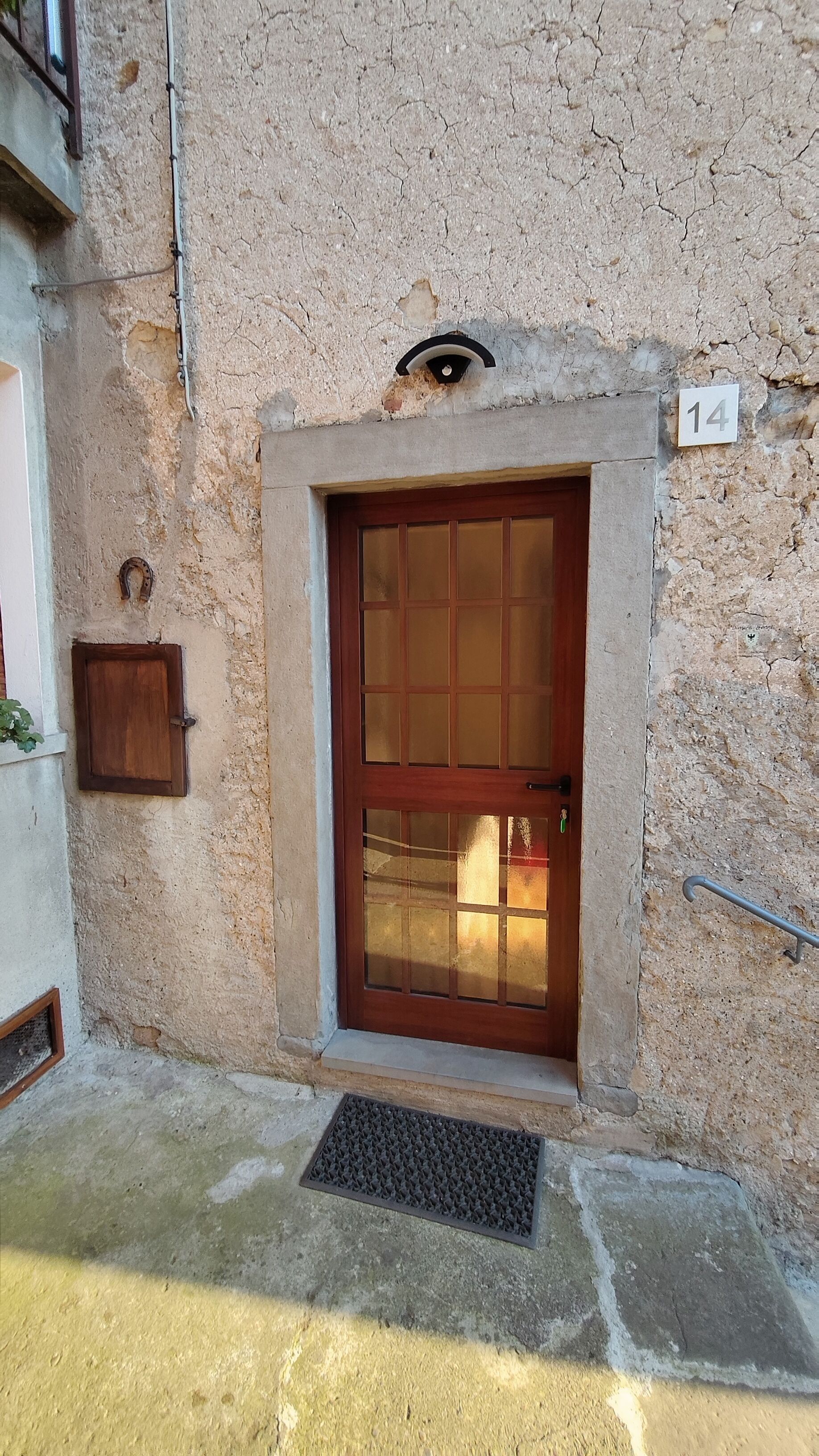 A building entrance with a wooden door, a small window, and a number plate.
