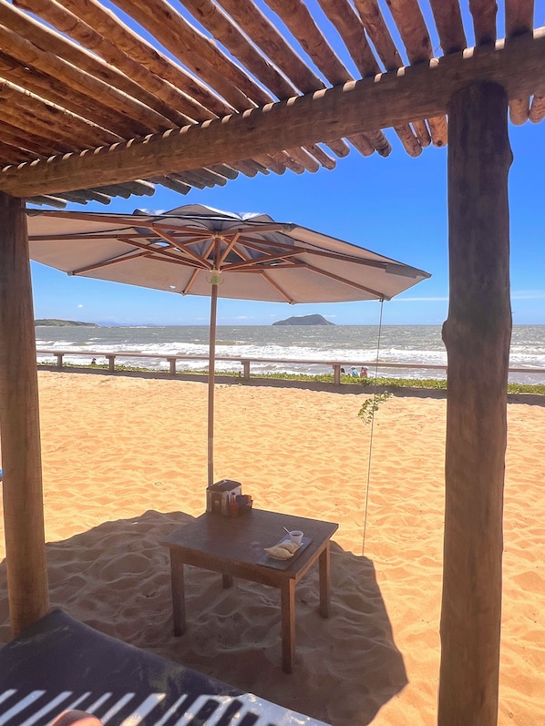 A beach umbrella, a table with a cup and a book, and a view of the ocean.