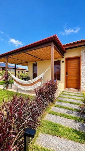A house with a red roof, a wooden door, and a hammock in the front yard.