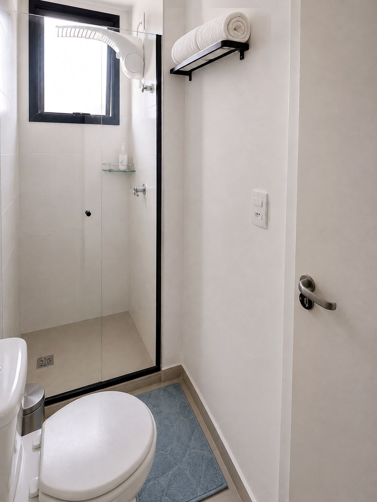 Un baño con inodoro, cabina de ducha de vidrio, perchero y ventana.