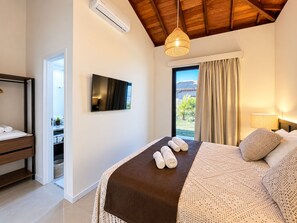 A bedroom with a bed, a television, a ceiling fan, and a view of the outdoors.