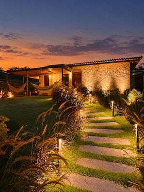 Una casa con fachada de piedra, una hamaca y un sendero iluminado en el jardín.