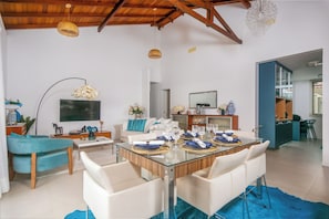 A modern living room with a glass dining table, white sofas, and a TV.