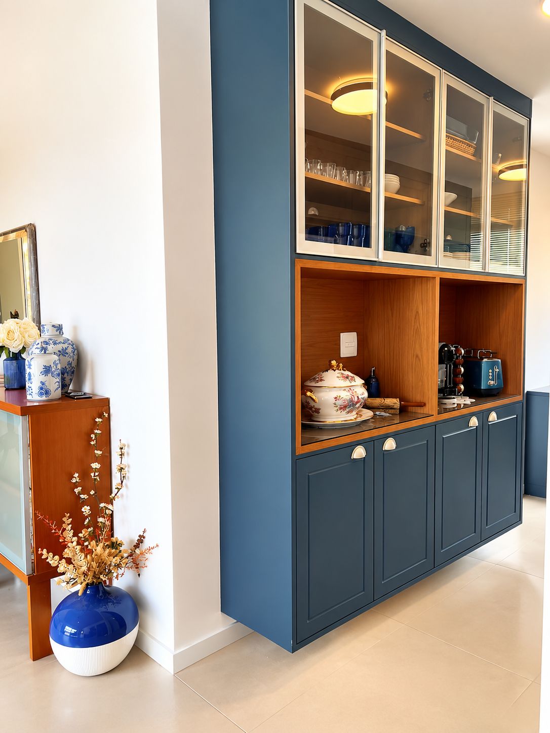 Una cocina moderna con armarios azules, encimera de madera y un mueble superior con puerta de vidrio que exhibe vajilla.
