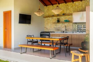 A compact kitchen with a stone backsplash, a built-in stove, and a sink. There is a wooden bench and chairs outside the kitchen area. - Villa Pérola do Aré · Heated and private Pool & Jacuzzi · Barbecue area (Armação dos Búzios)