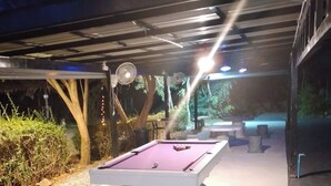Un espace extérieur avec une piscine, une table de billard, des sièges et une zone abritée.
