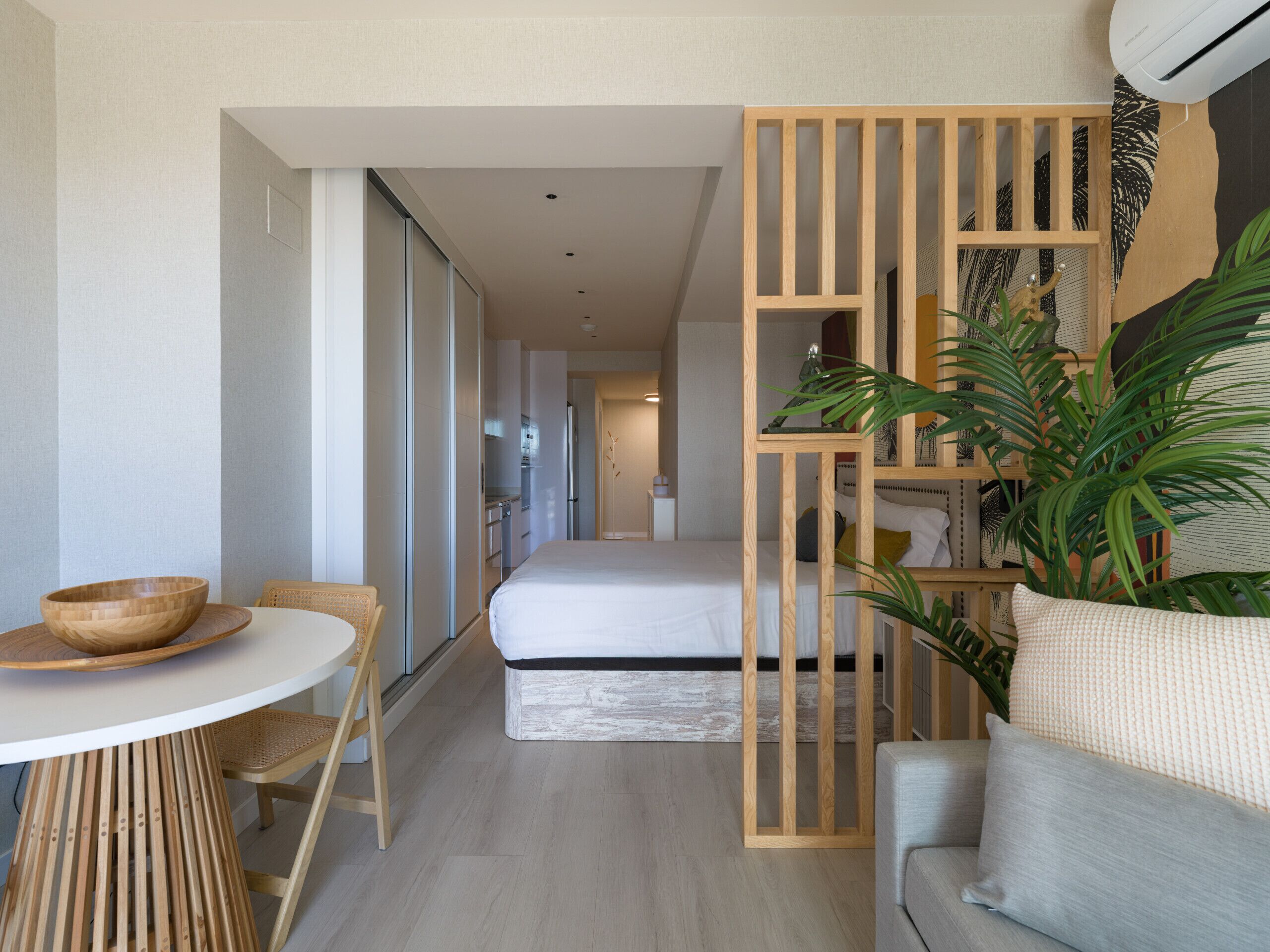 Ein moderner, kompakter Wohnraum mit Küchenzeile, einem Essbereich mit Holztisch und Stühlen, einer Couch und einer großen Küstpflanze.