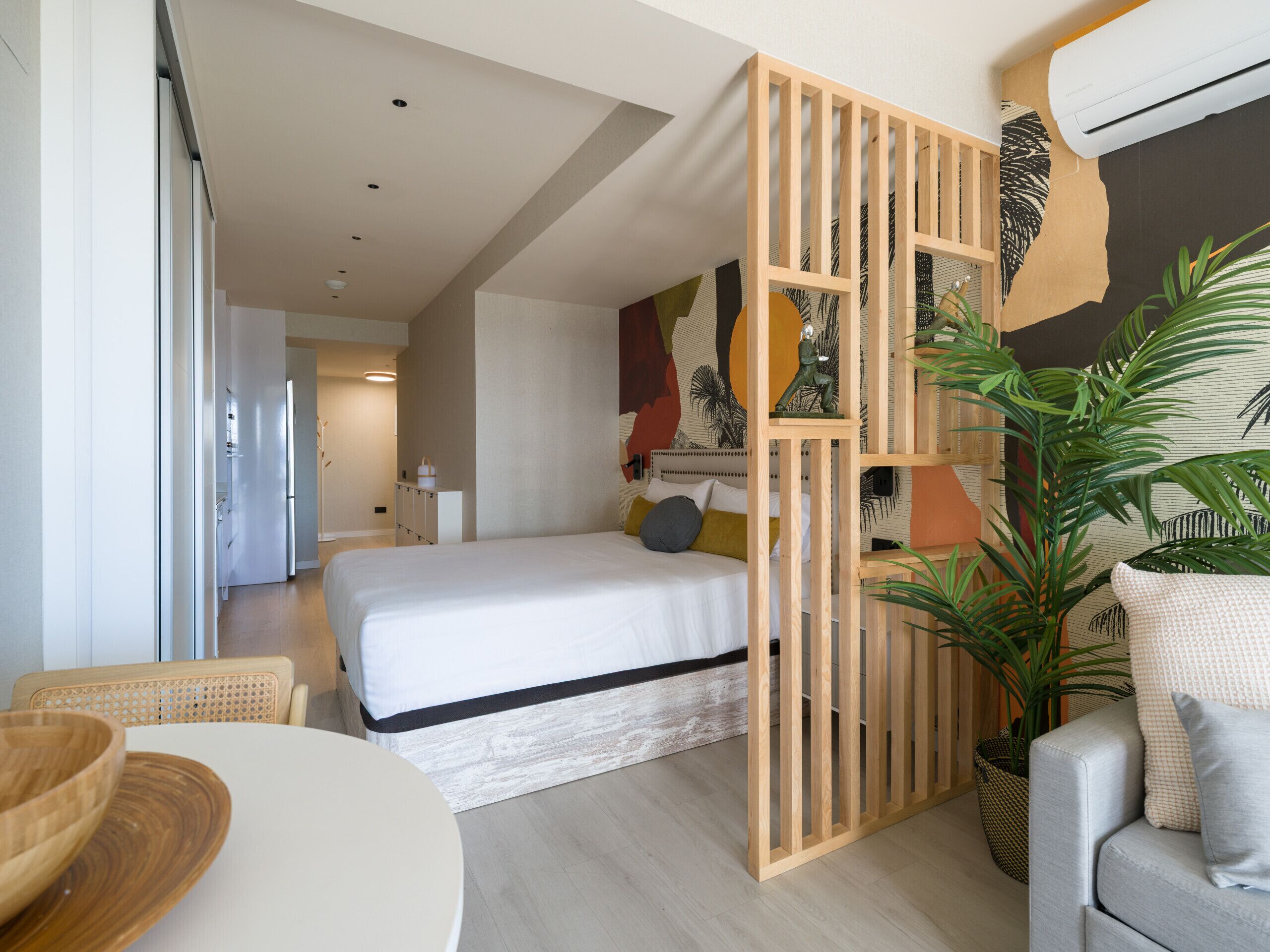 Quarto moderno com cama, divisória de madeira, planta em vaso e área de jantar com mesa e cadeiras.