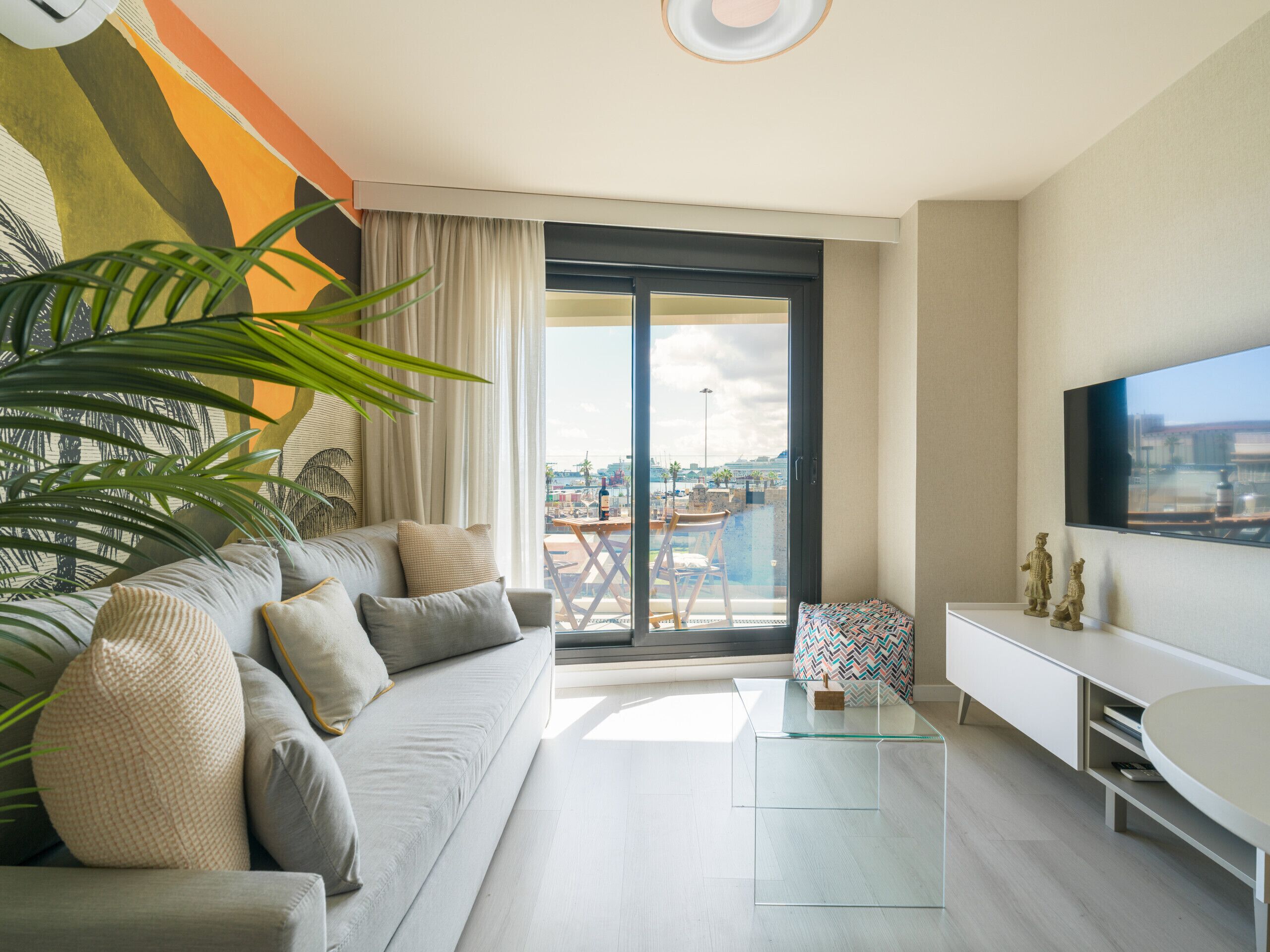 Un salon moderne avec un canapé, une table basse en verre et un téléviseur fixé au mur.