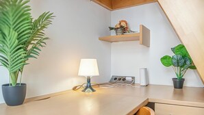 A modern room with a wooden table, a desk lamp, a potted plant, a shelf with flowers, and a power outlet. - Bright Apartment Near Wiener Stadthalle (Vienna)