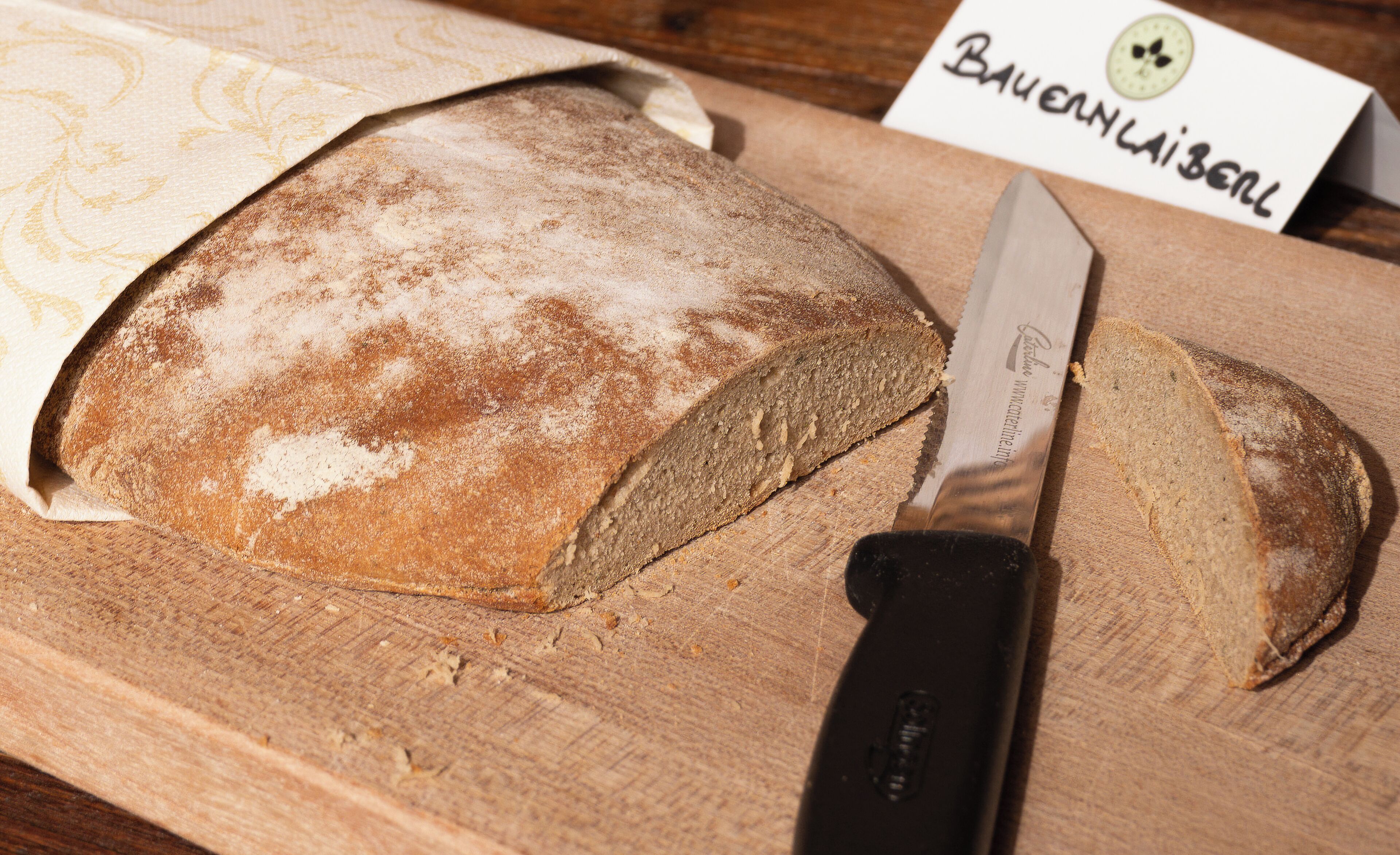 Une miche de pain sur une planche à découper en bois, avec un couteau et une étiquette indiquant « Bauernladen ».