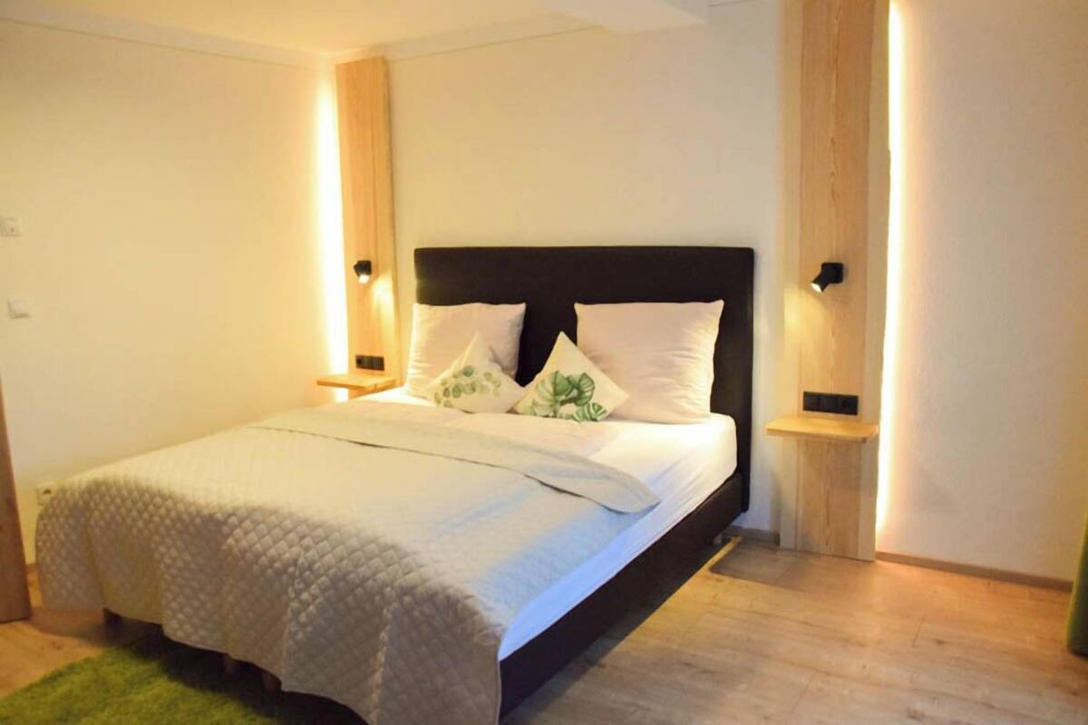 A bedroom with a bed, bedside lamps, a green rug, and a wooden nightstand.