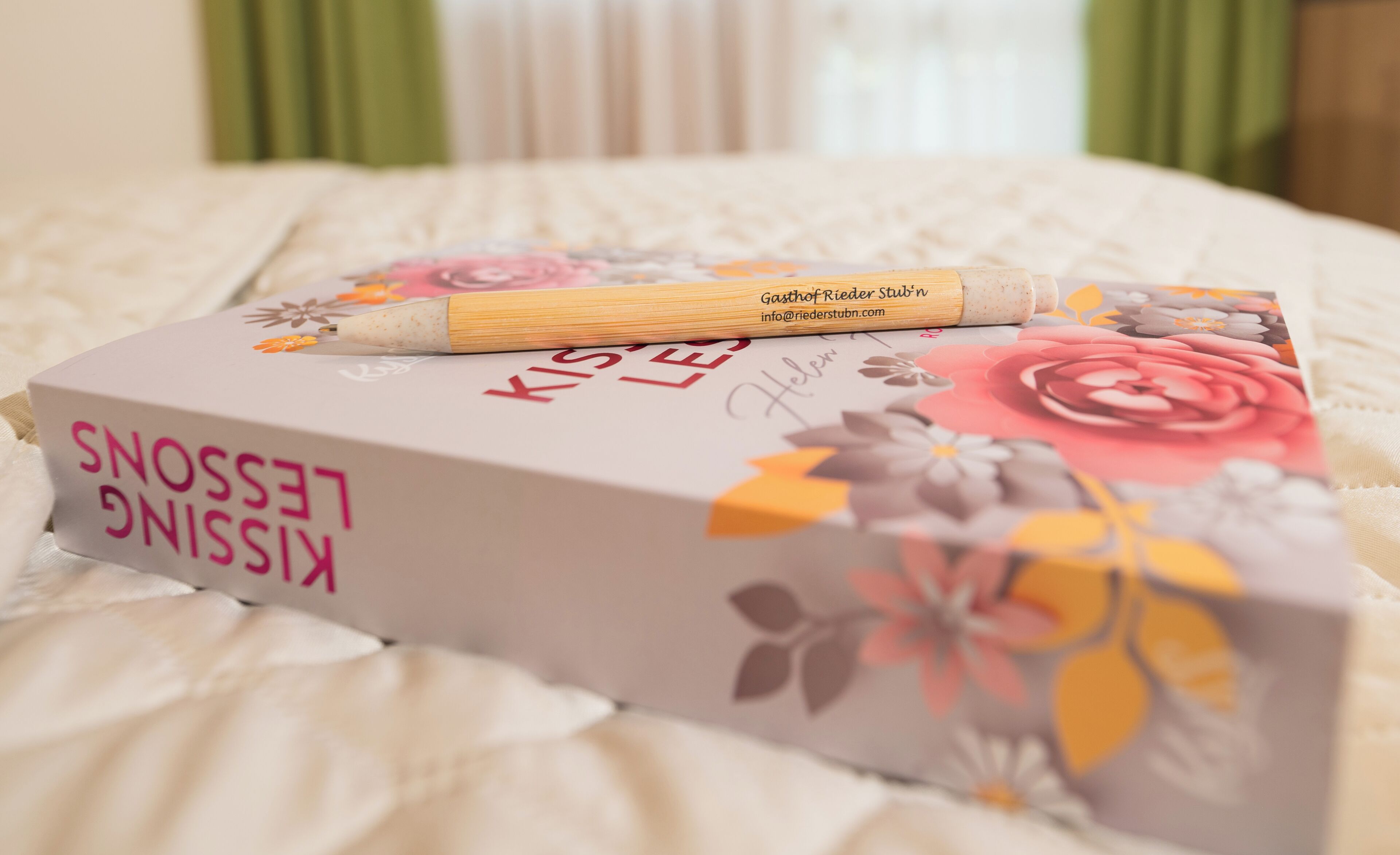 Ein Buch mit dem Titel 'Kissling Lesse' auf einem Bett, dessen Bezug ein Blumenmuster aufweist.