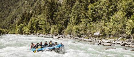 A group of people in a blue raft navigating a river surrounded by forested hills.