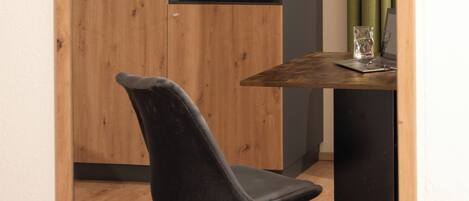 A room with a wooden cabinet, a black chair, a small table with a glass, and a green curtain.