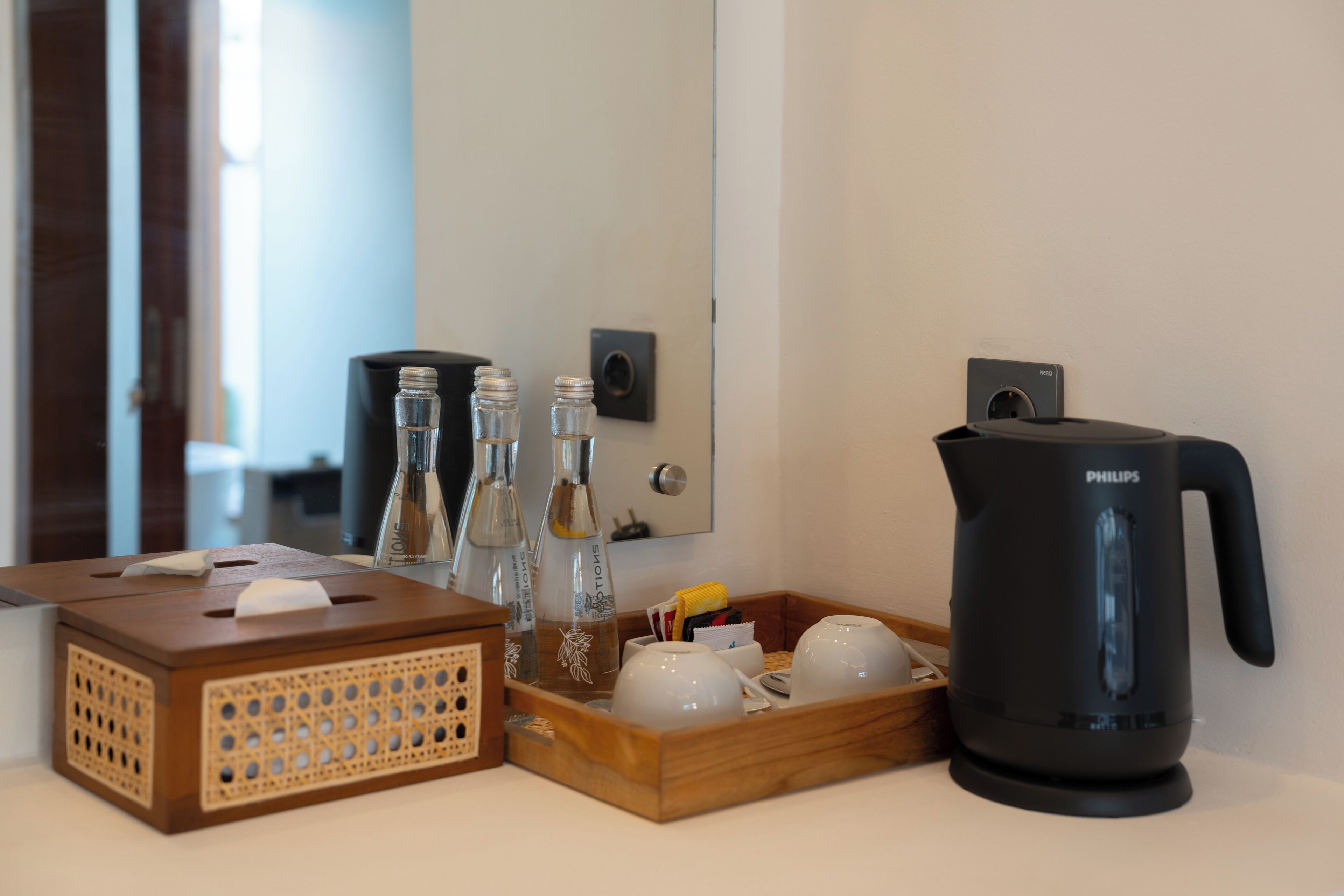 A hotel room's reception area with a wooden tissue box, a tray with bottles and glasses, and a black Philips coffee maker.