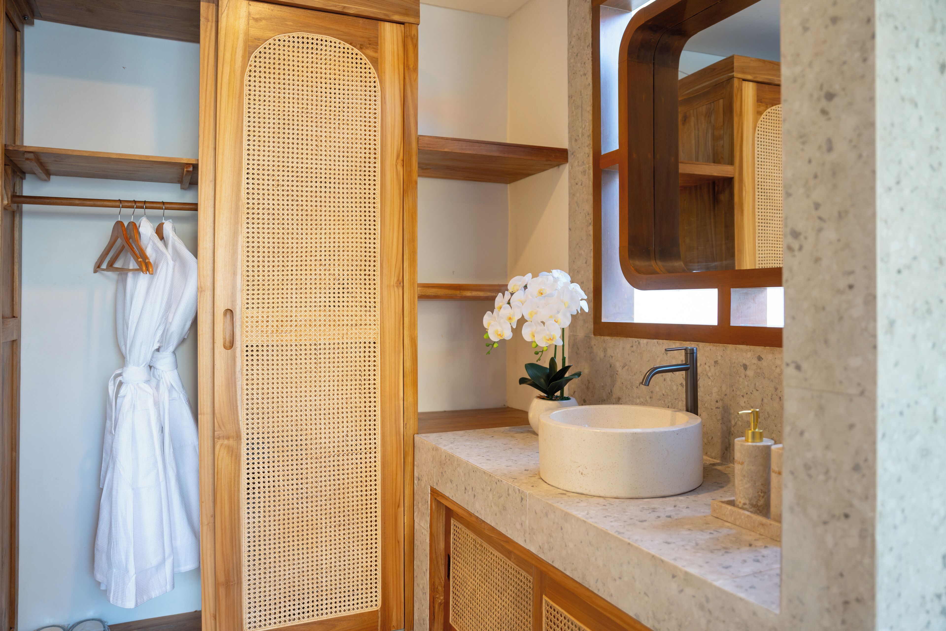 A bathroom with a wooden vanity, a round sink, a mirror, and a white robe hanging on a rack.