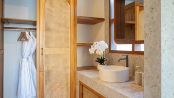 A bathroom with a wooden vanity, a round sink, a mirror, and a white robe hanging on a rack.