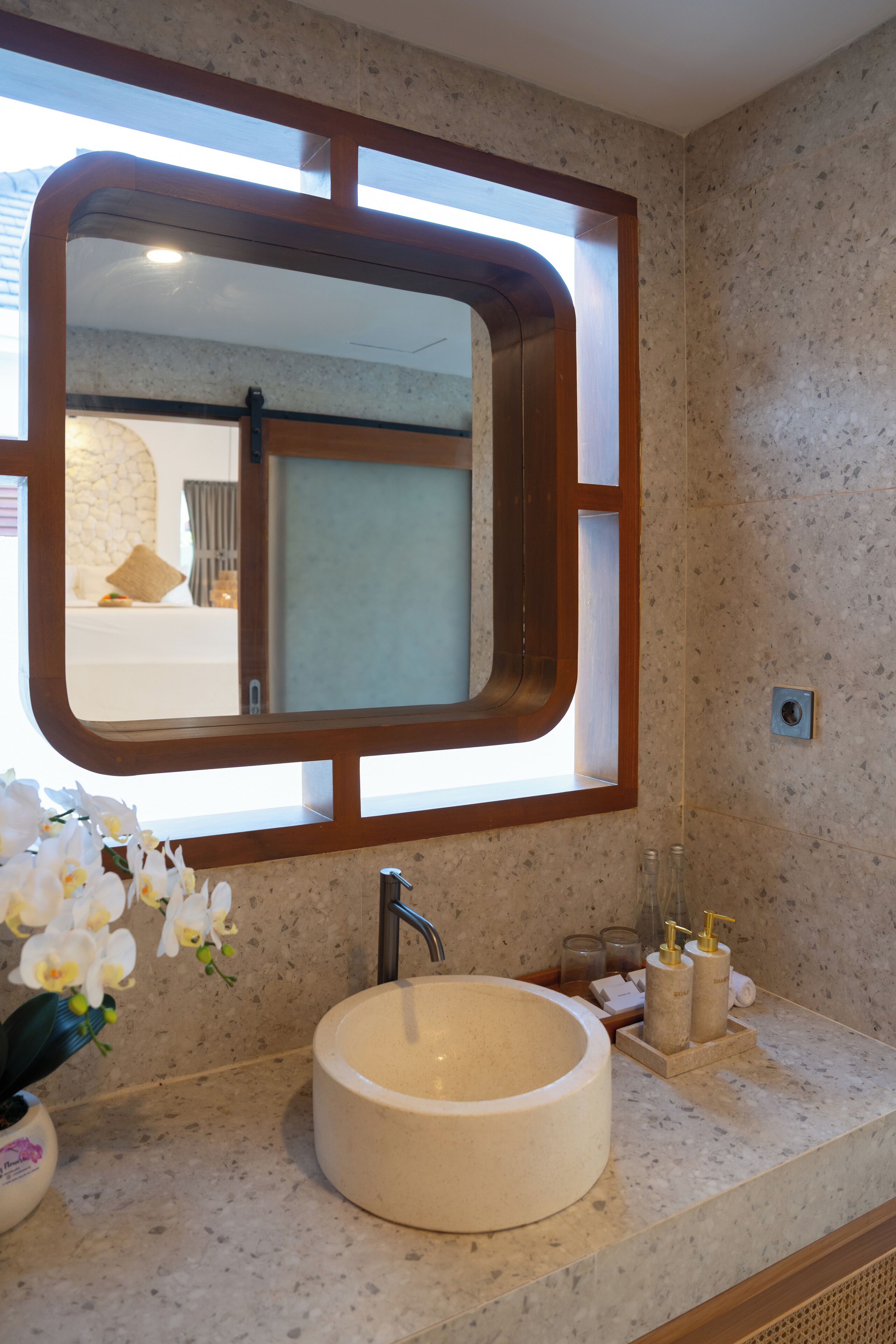A bathroom with a large mirror, a round sink, and a vase of flowers.