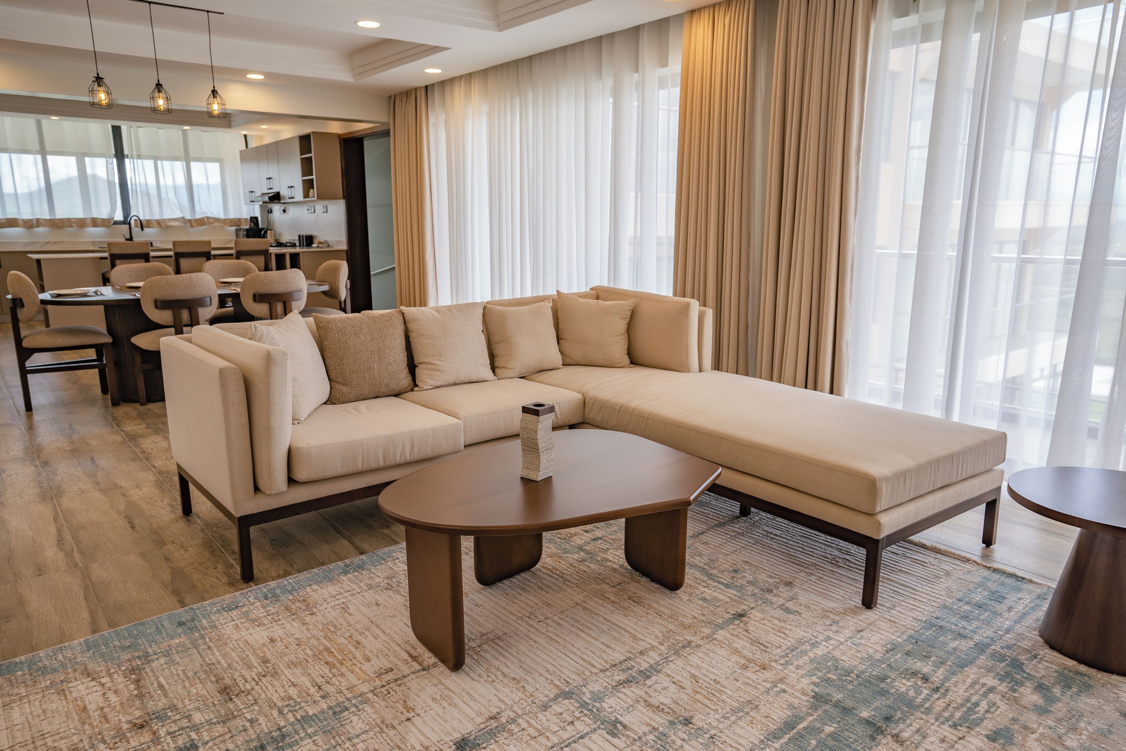 Een moderne woonkamer met een grote L-vormige zithoek, een ronde salontafel en een eethoek op de achtergrond.