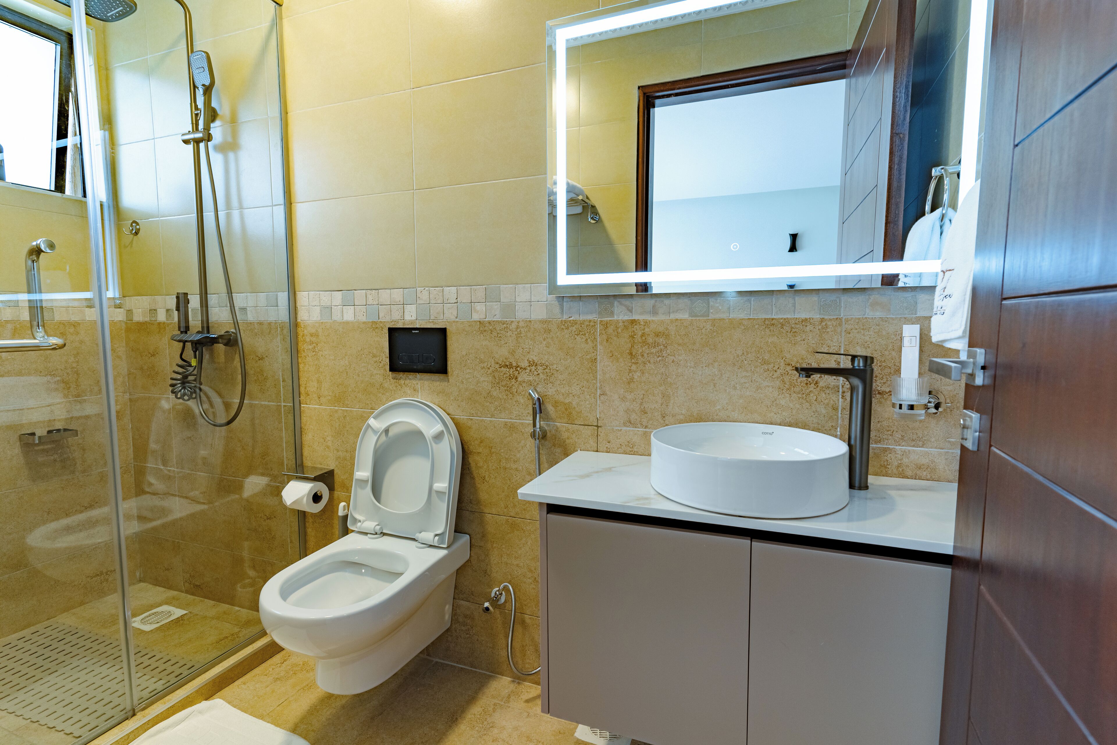 A modern bathroom with a glass-enclosed shower, a toilet with a raised seat, and a vanity with a sink and mirror.
