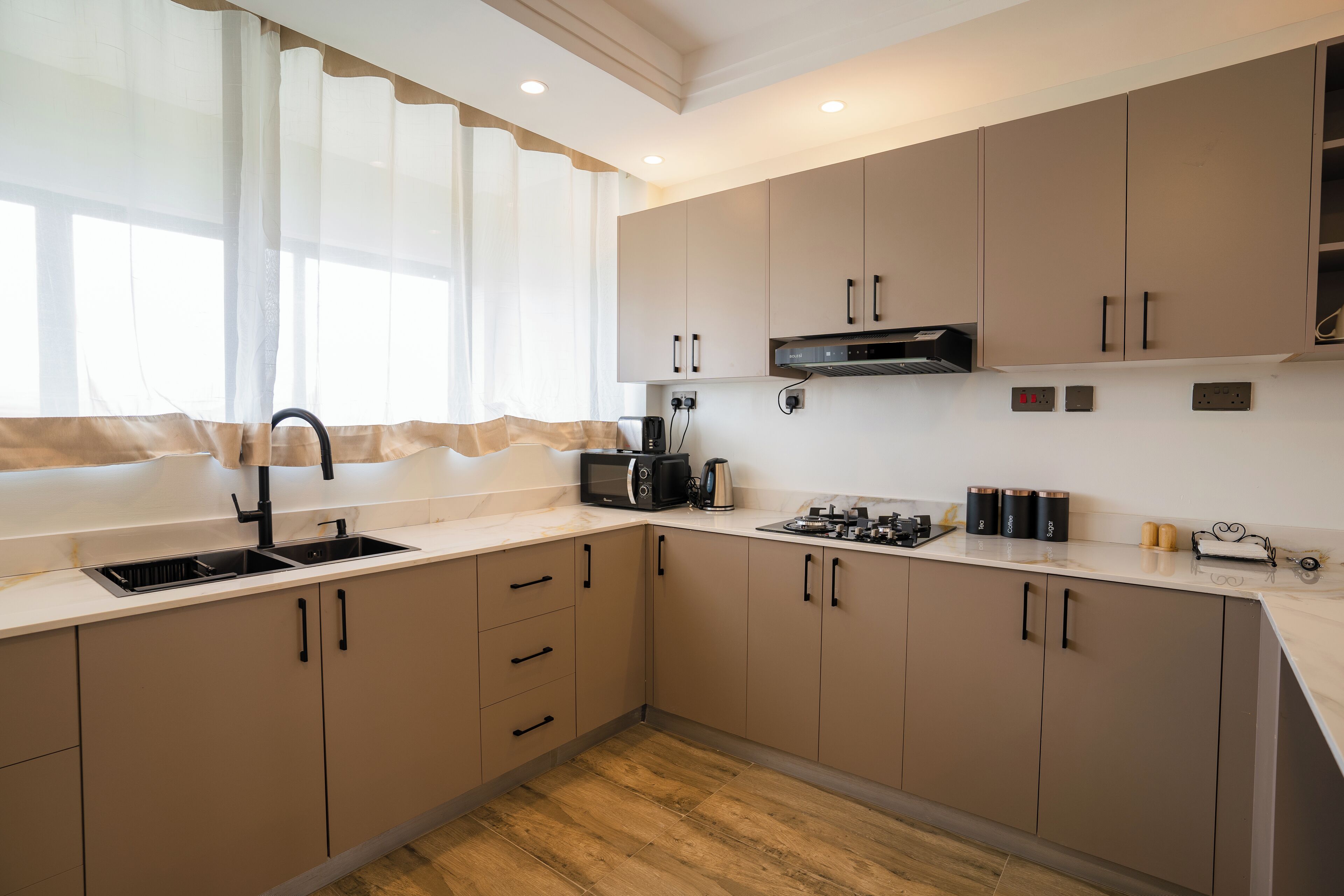 A modern kitchen with beige cabinets, a sink, a microwave, and a stove.