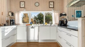 Una cocina moderna con armarios blancos, lavavajillas y un ventanal con cortinas.