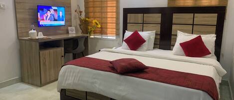 Una habitación de hotel con cama, escritorio, televisión y ventana con persianas.