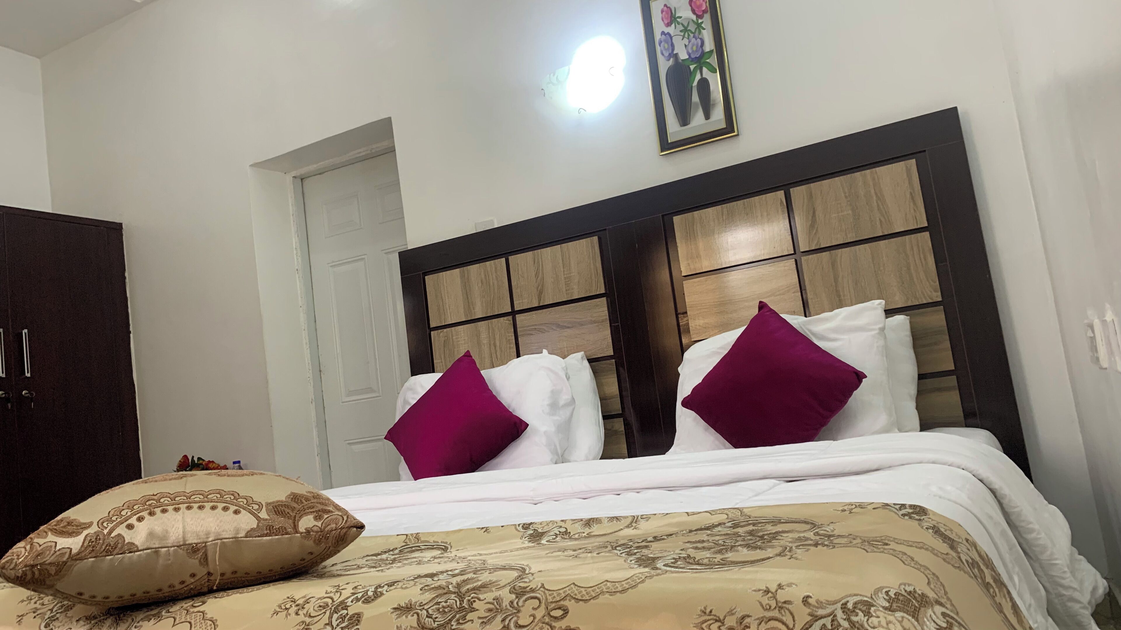 A hotel room with a bed, a wooden headboard, and a door.