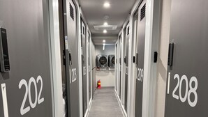 Een hotelgang met kluisjes met de nummers 202 en 208, een brandblusser en een plafondlamp.