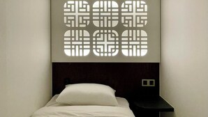 Een moderne hotelkamer met een netjes opgemaakt bed, een donker hoofdeinde en een wandlamp.