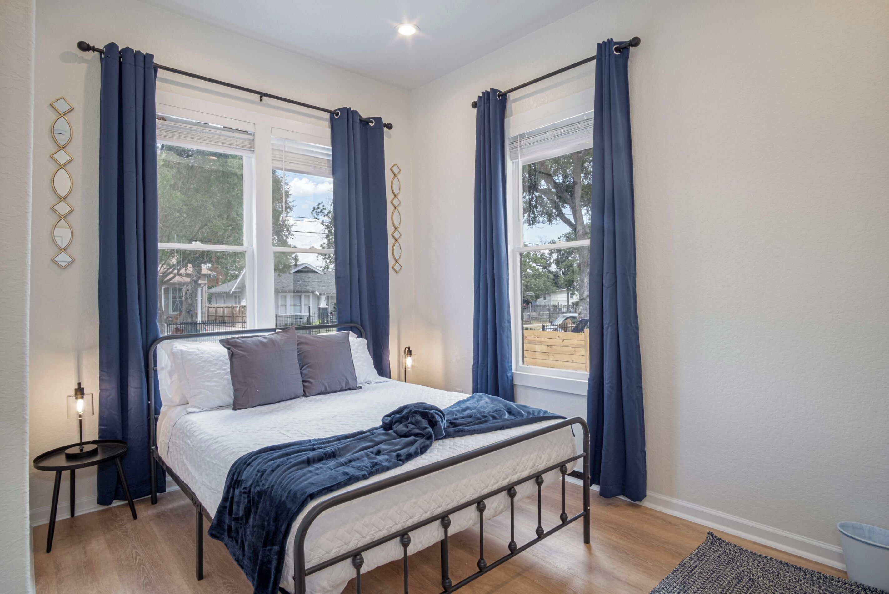 Une chambre à coucher avec un lit, des rideaux, une table de chevet et une vue sur l’extérieur.