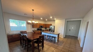 A spacious kitchen with a central island, wooden cabinets, and a dining area with four chairs. - Cozy 4bd3ba Pool/FirePit/BBQ House in Maricopa (Maricopa)